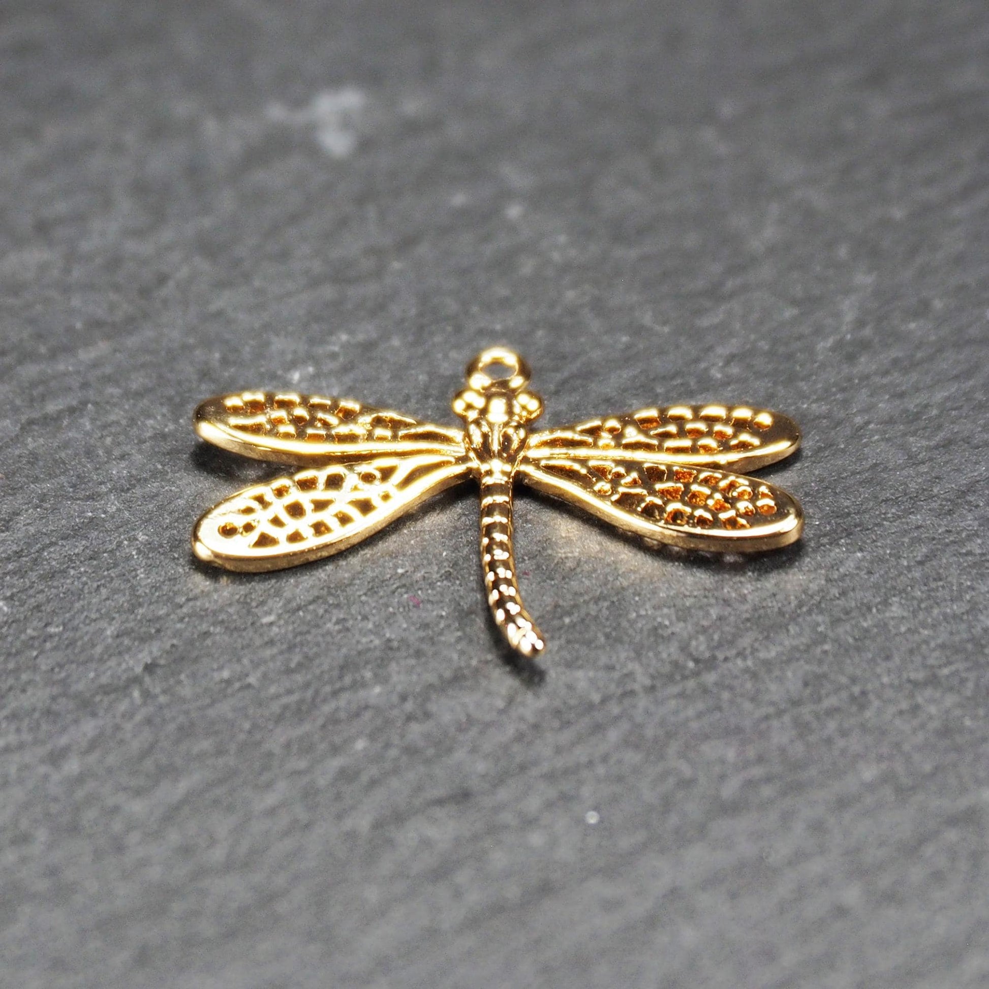 Libellen-Anhänger aus goldfarbenem, glänzendem Metall mit durchbrochenen, netzartigen Flügeln, schlankem segmentiertem Körper und kleiner runder Aufhängöse.