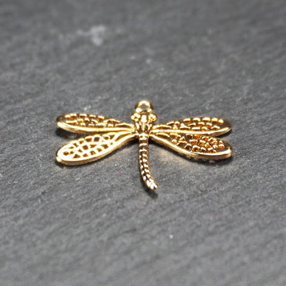 Libellen-Anhänger aus goldfarbenem, glänzendem Metall mit durchbrochenen, netzartigen Flügeln, schlankem segmentiertem Körper und kleiner runder Aufhängöse.