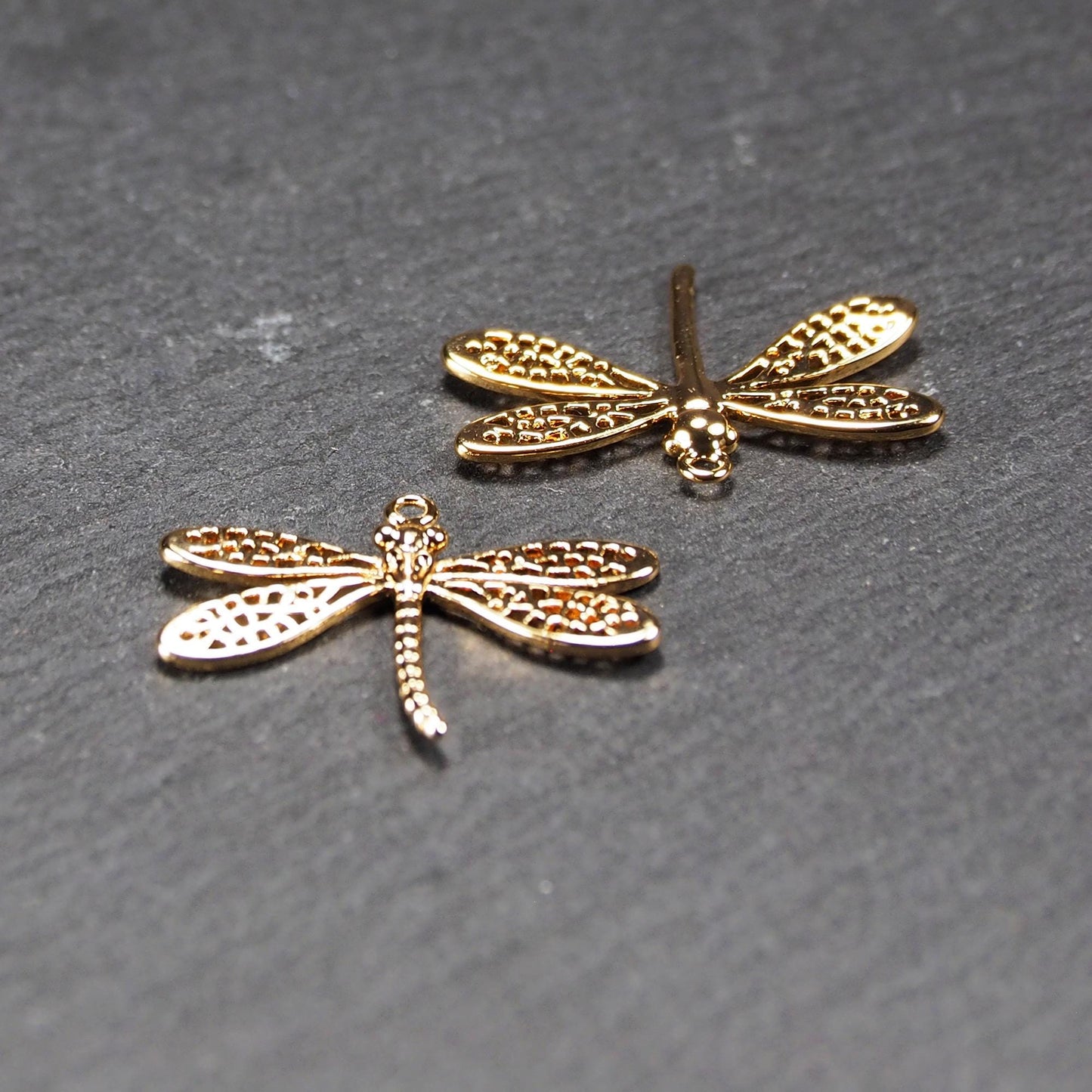 Libellen-Anhänger (Vorder- und Rückseite) aus goldfarbenem, glänzendem Metall mit durchbrochenen, netzartigen Flügeln, schlankem segmentiertem Körper und kleiner runder Aufhängöse.