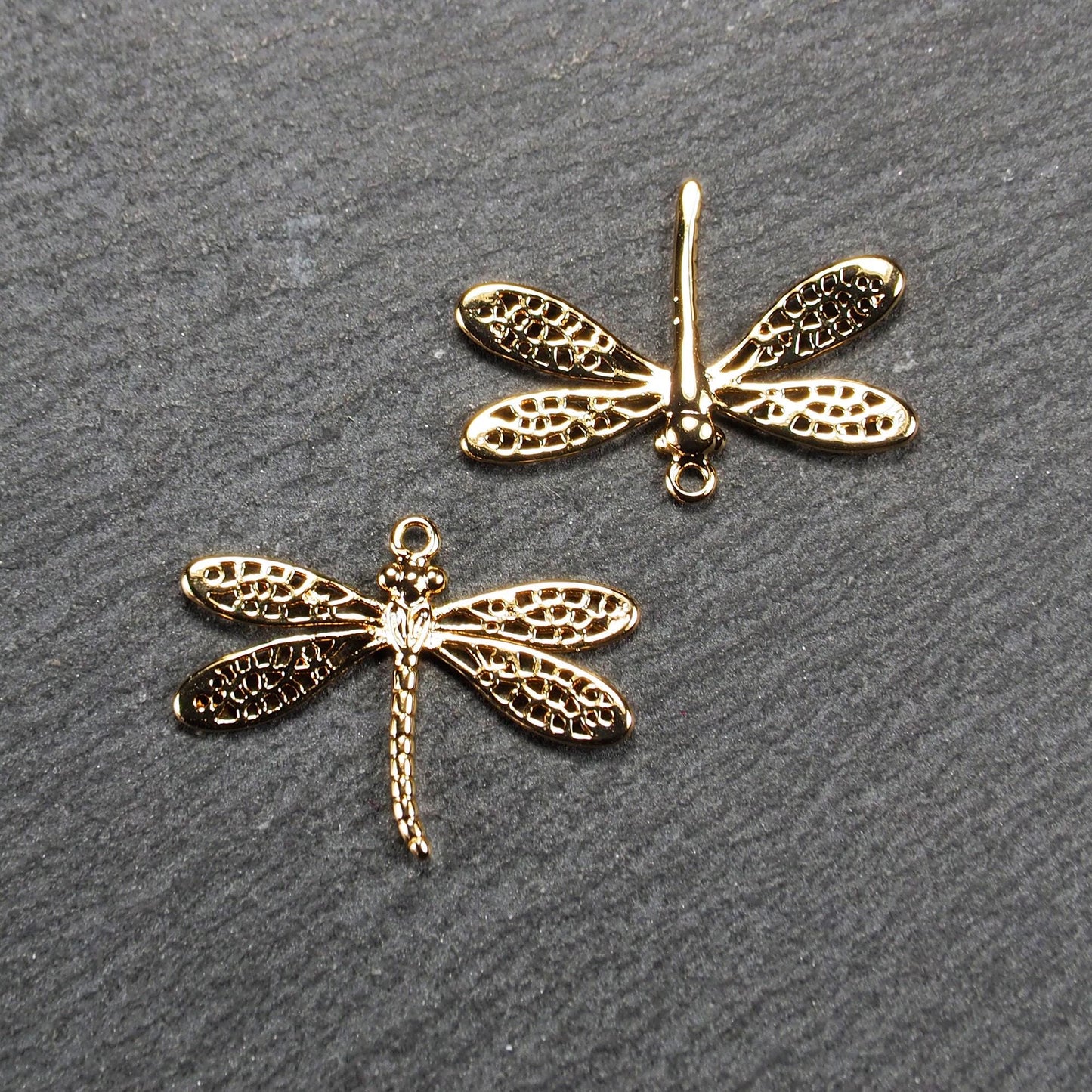 Libellen-Anhänger (Vorder- und Rückseite) aus goldfarbenem, glänzendem Metall mit durchbrochenen, netzartigen Flügeln, schlankem segmentiertem Körper und kleiner runder Aufhängöse.