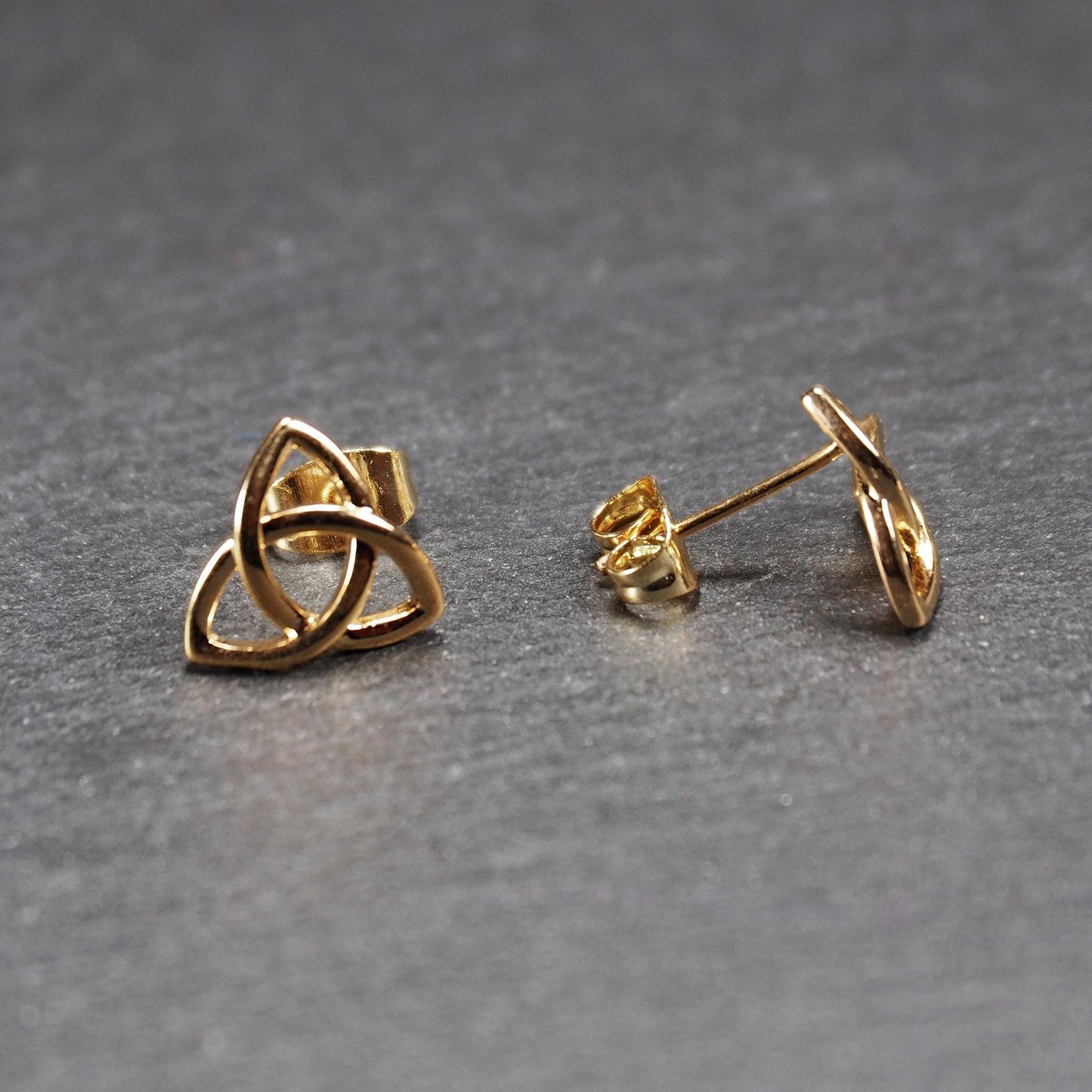 Paar goldfarbener Ohrstecker mit offen gearbeitetem Triquetra-Knoten, glänzende Oberfläche und sichtbaren Schmetterlingsverschlüssen.