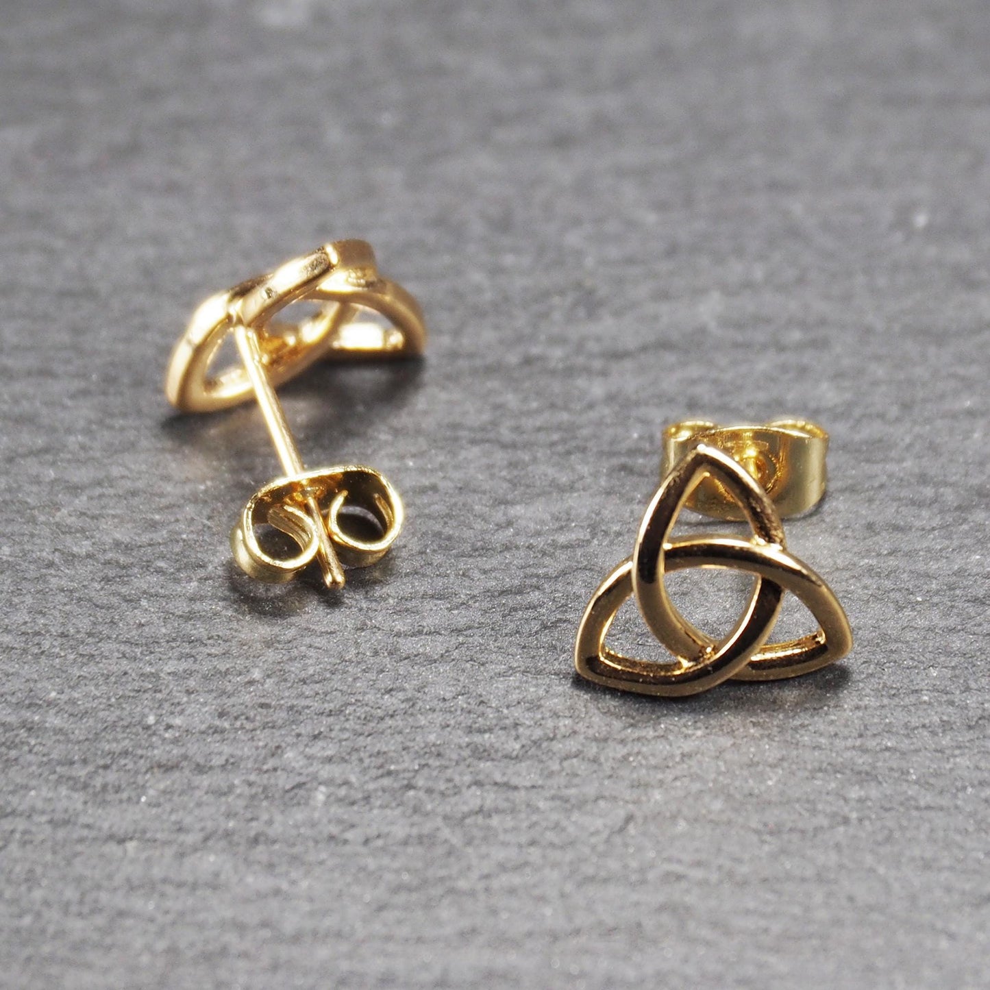 Paar goldfarbener Ohrstecker mit offen gearbeitetem Triquetra-Knoten, glänzende Oberfläche und sichtbaren Schmetterlingsverschlüssen.