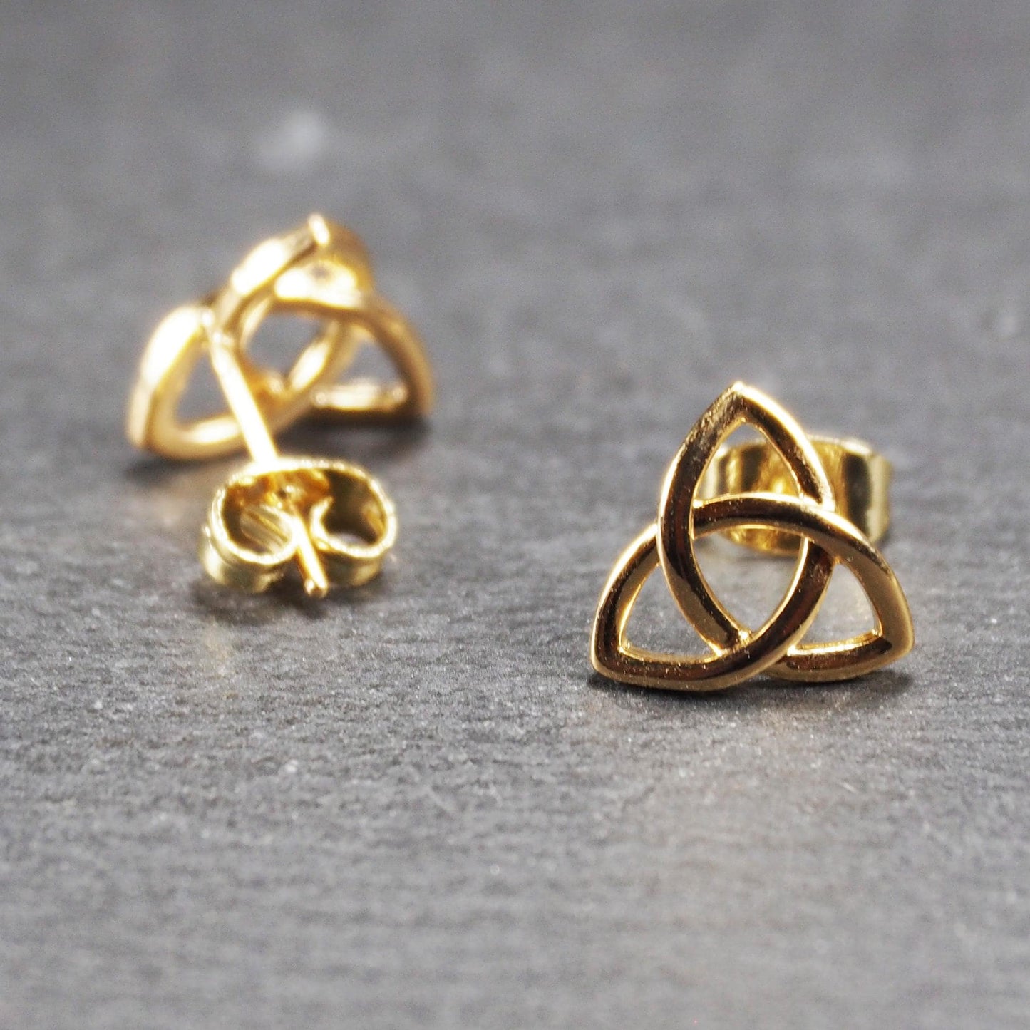 Paar goldfarbener Ohrstecker mit offen gearbeitetem Triquetra-Knoten, glänzende Oberfläche und sichtbaren Schmetterlingsverschlüssen.