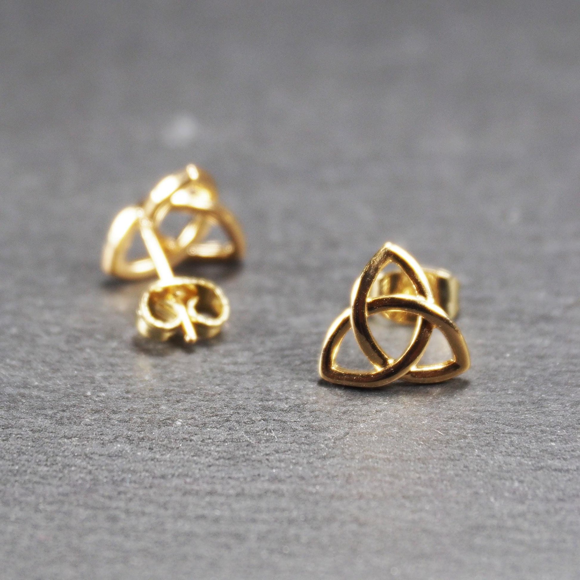Paar goldfarbener Ohrstecker mit offen gearbeitetem Triquetra-Knoten, glänzende Oberfläche und sichtbaren Schmetterlingsverschlüssen.