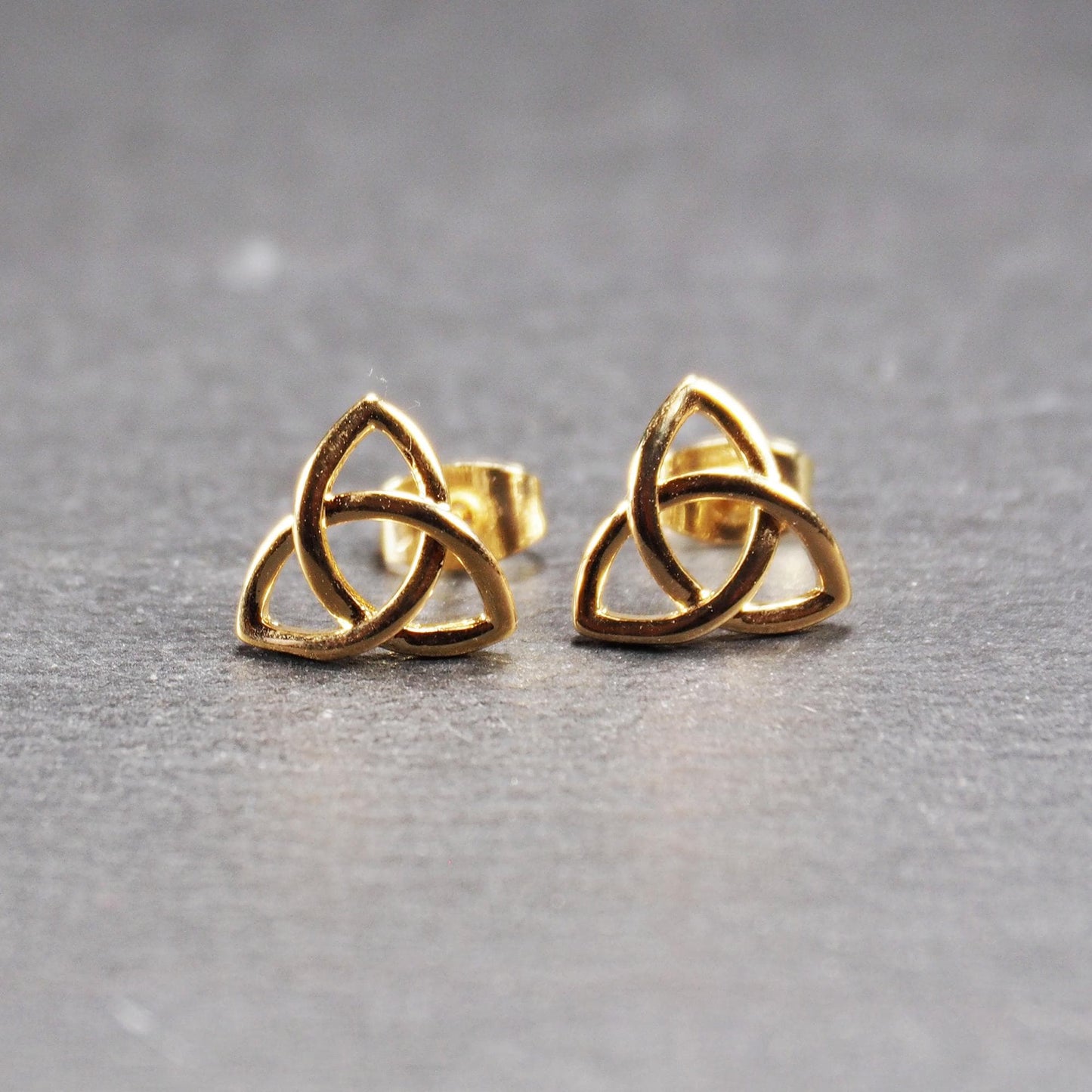 Paar goldfarbener Ohrstecker mit offen gearbeitetem Triquetra-Knoten, glänzende Oberfläche und sichtbaren Schmetterlingsverschlüssen.