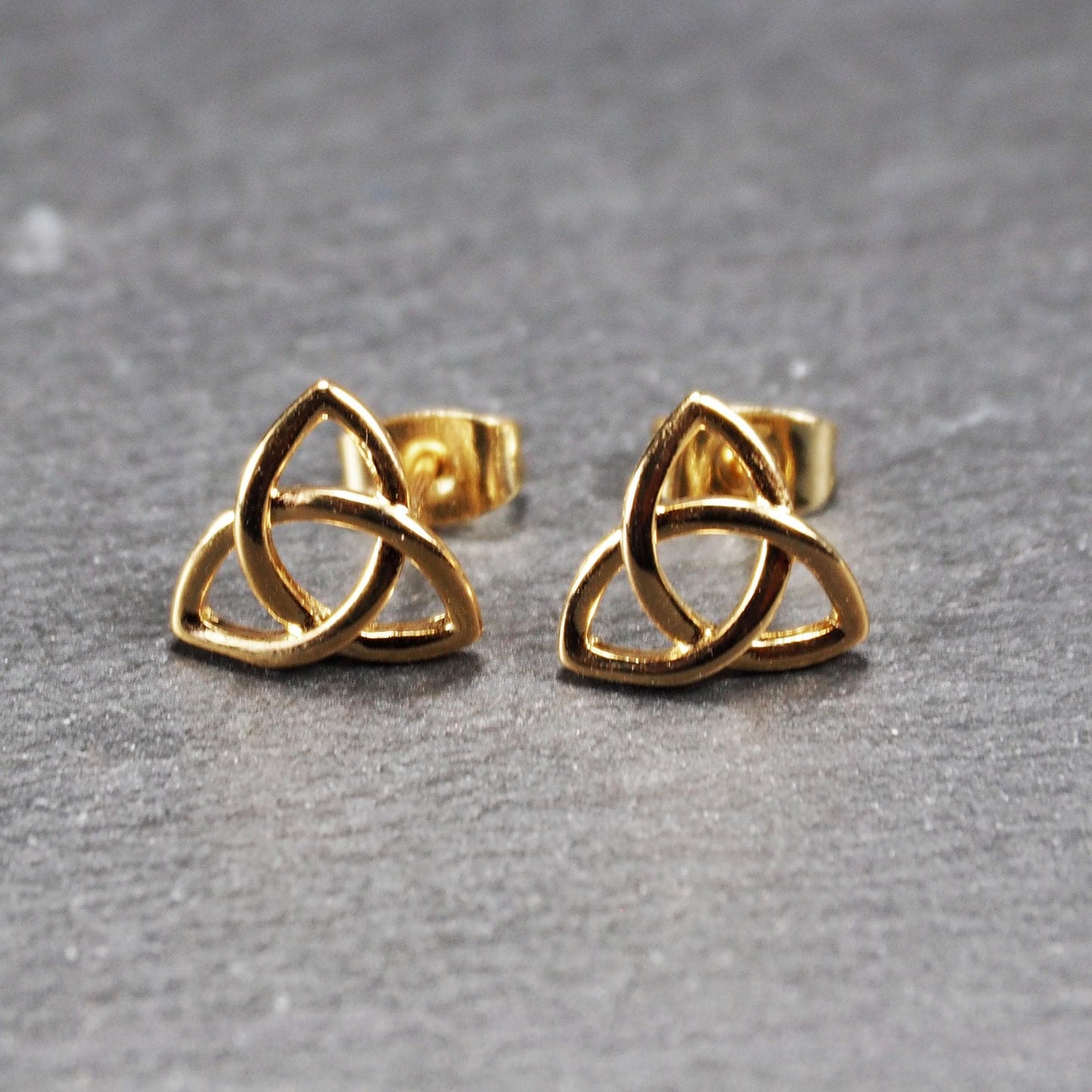Paar goldfarbener Ohrstecker mit offen gearbeitetem Triquetra-Knoten, glänzende Oberfläche und sichtbaren Schmetterlingsverschlüssen.