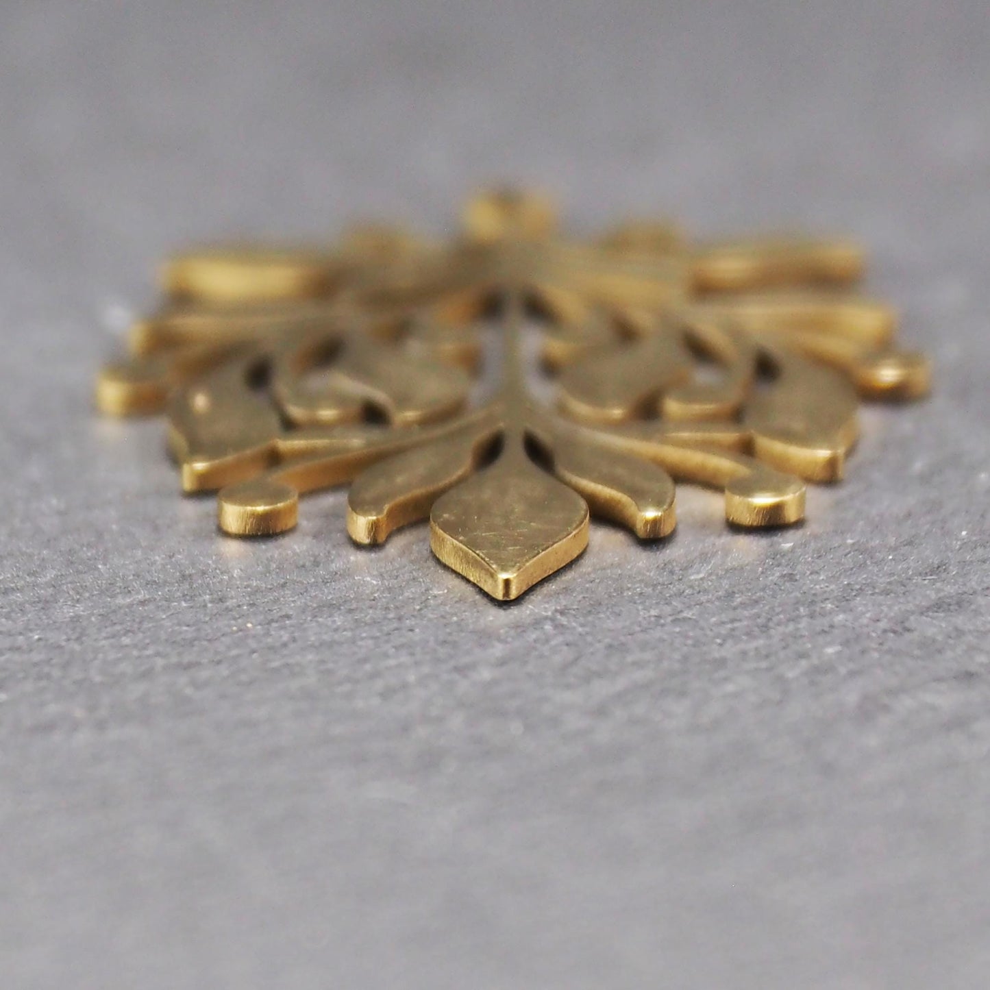 Goldfarbener Metallanhänger mit glänzender Oberfläche, durchbrochenes Zweig- und Beerenmotiv mit stilisierten Blättern und runder Öse oben.