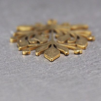 Goldfarbener Metallanhänger mit glänzender Oberfläche, durchbrochenes Zweig- und Beerenmotiv mit stilisierten Blättern und runder Öse oben.