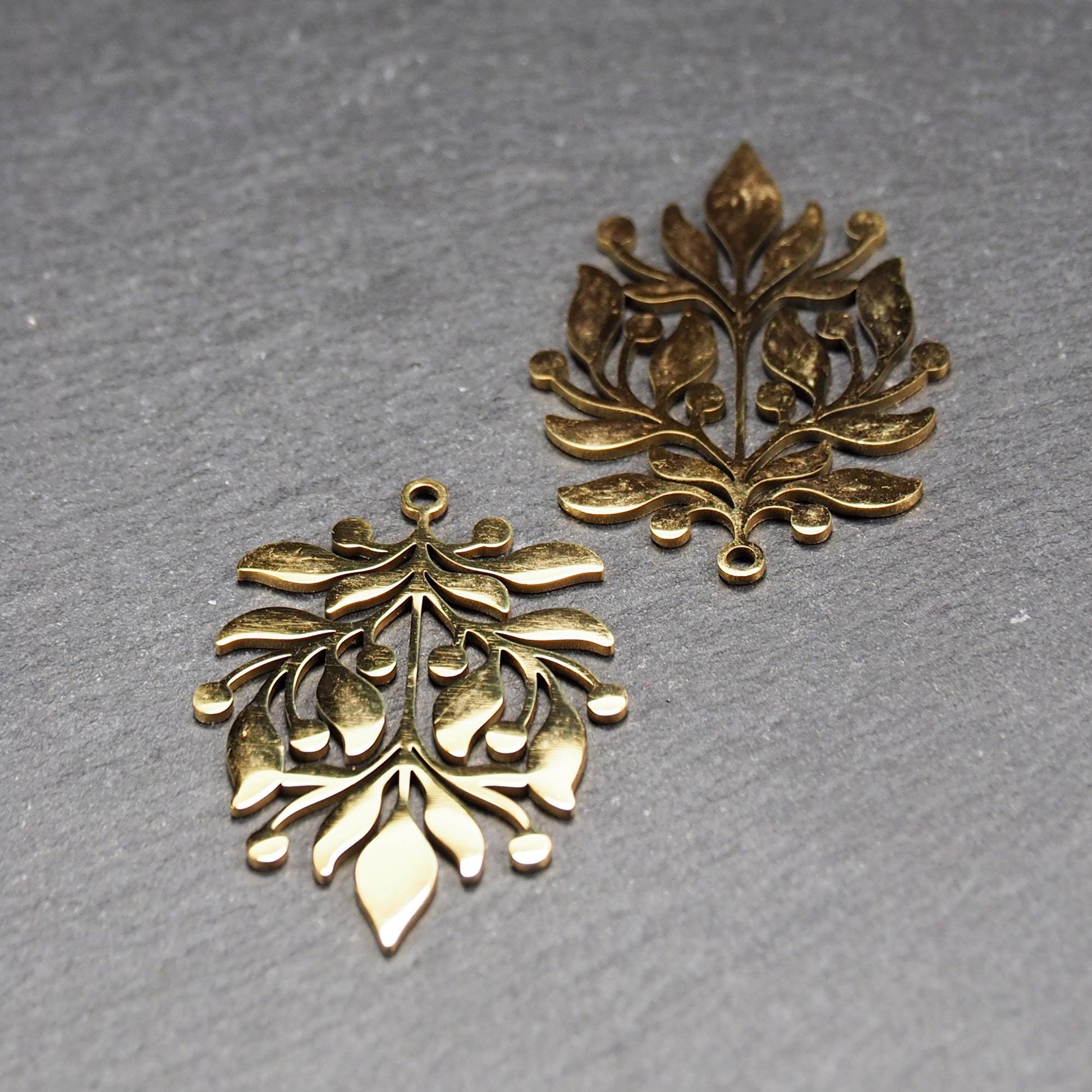 Goldfarbener Metallanhänger mit glänzender Oberfläche, durchbrochenes Zweig- und Beerenmotiv mit stilisierten Blättern und runder Öse oben.