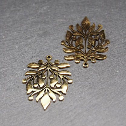 Goldfarbener Metallanhänger mit glänzender Oberfläche, durchbrochenes Zweig- und Beerenmotiv mit stilisierten Blättern und runder Öse oben.