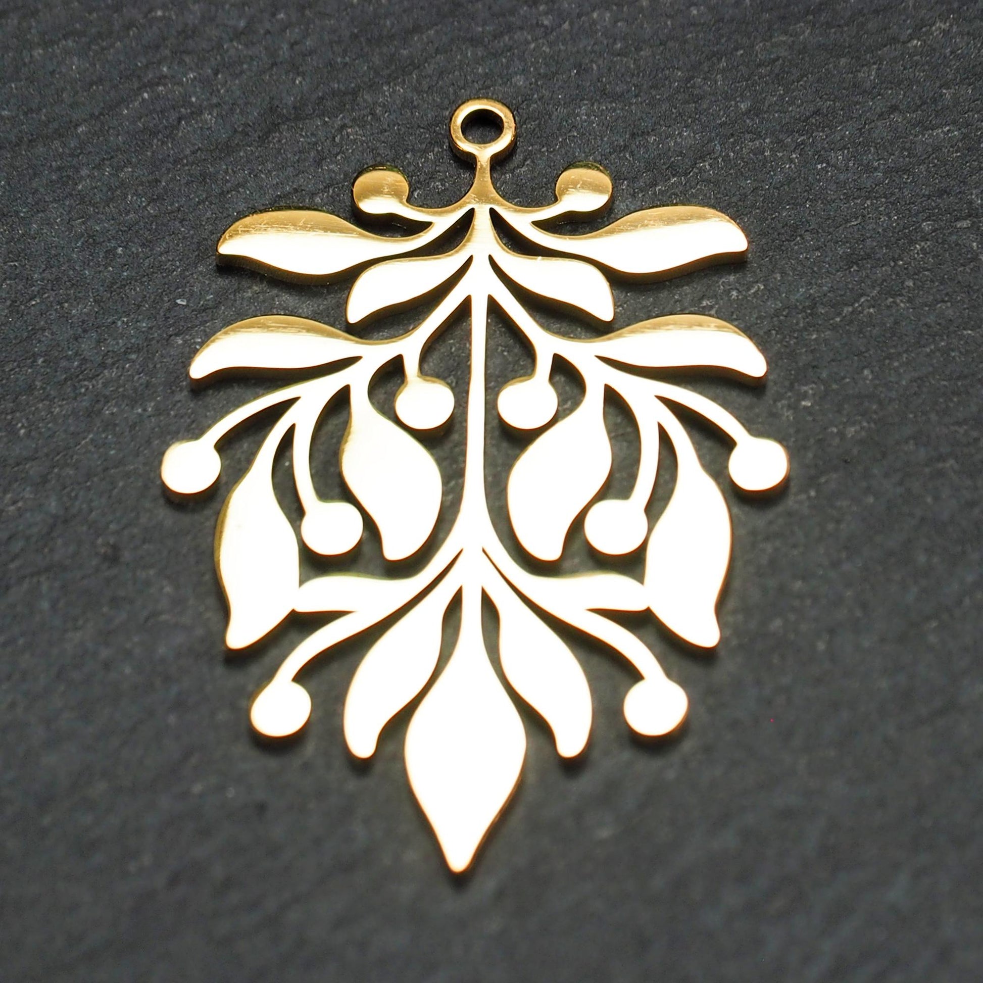 Goldfarbener Metallanhänger mit glänzender Oberfläche, durchbrochenes Zweig- und Beerenmotiv mit stilisierten Blättern und runder Öse oben.