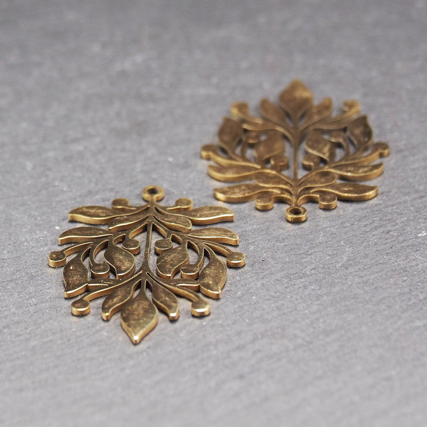 Goldfarbener Metallanhänger mit glänzender Oberfläche, durchbrochenes Zweig- und Beerenmotiv mit stilisierten Blättern und runder Öse oben.