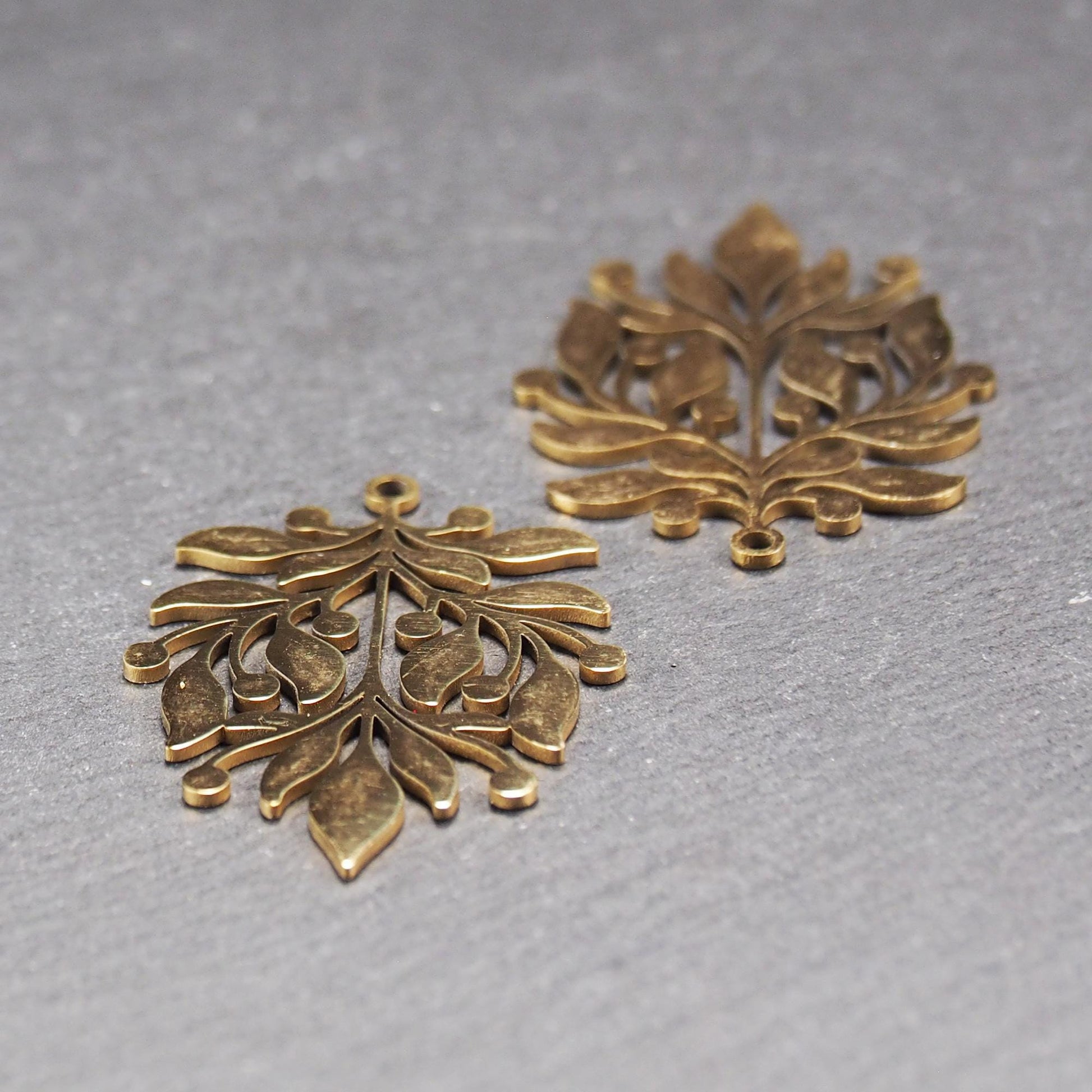 Goldfarbener Metallanhänger mit glänzender Oberfläche, durchbrochenes Zweig- und Beerenmotiv mit stilisierten Blättern und runder Öse oben.