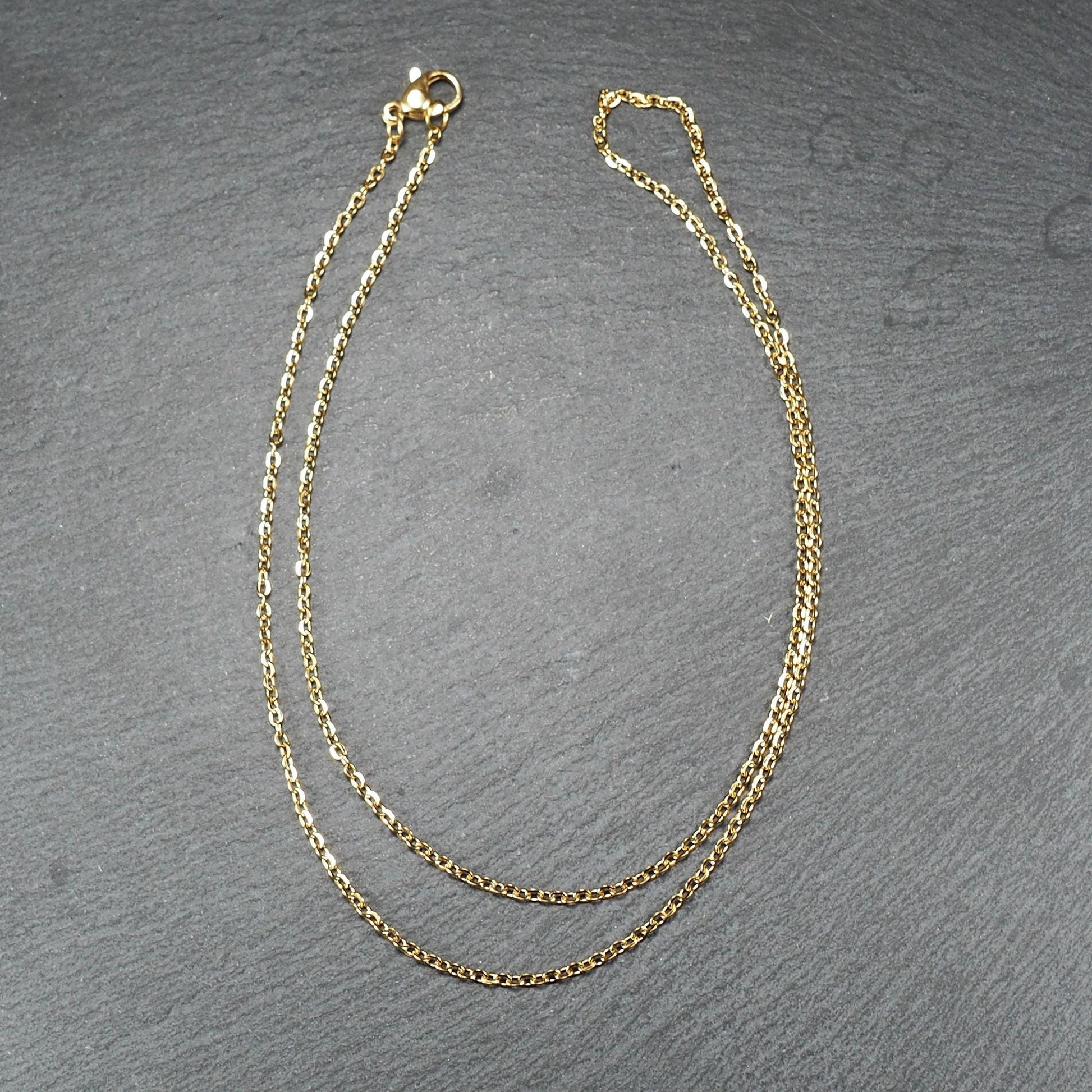 Feine goldfarbene Ankerkette mit glänzender Oberfläche, filigranen ovalen Gliedern in Spiralform und sichtbarem Karabinerverschluss.