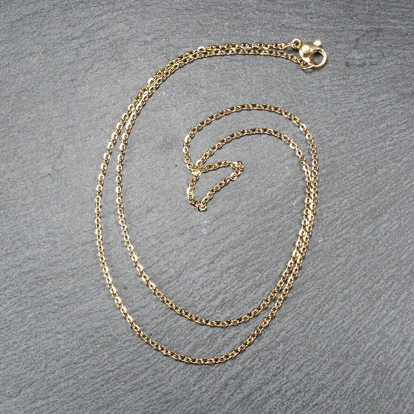 Feine goldfarbene Ankerkette mit glänzender Oberfläche, filigranen ovalen Gliedern in Spiralform und sichtbarem Karabinerverschluss.