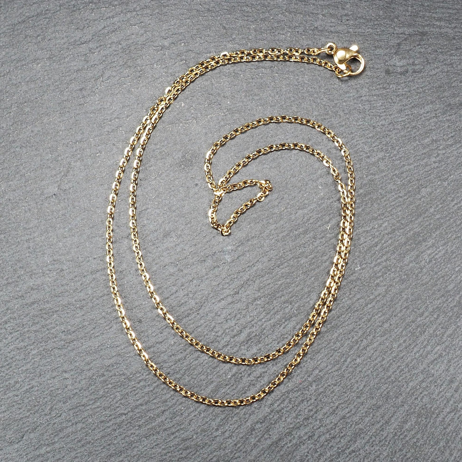 Feine goldfarbene Ankerkette mit glänzender Oberfläche, filigranen ovalen Gliedern in Spiralform und sichtbarem Karabinerverschluss.