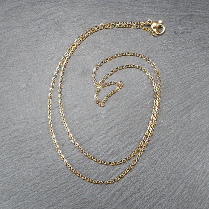 Feine goldfarbene Ankerkette mit glänzender Oberfläche, filigranen ovalen Gliedern in Spiralform und sichtbarem Karabinerverschluss.