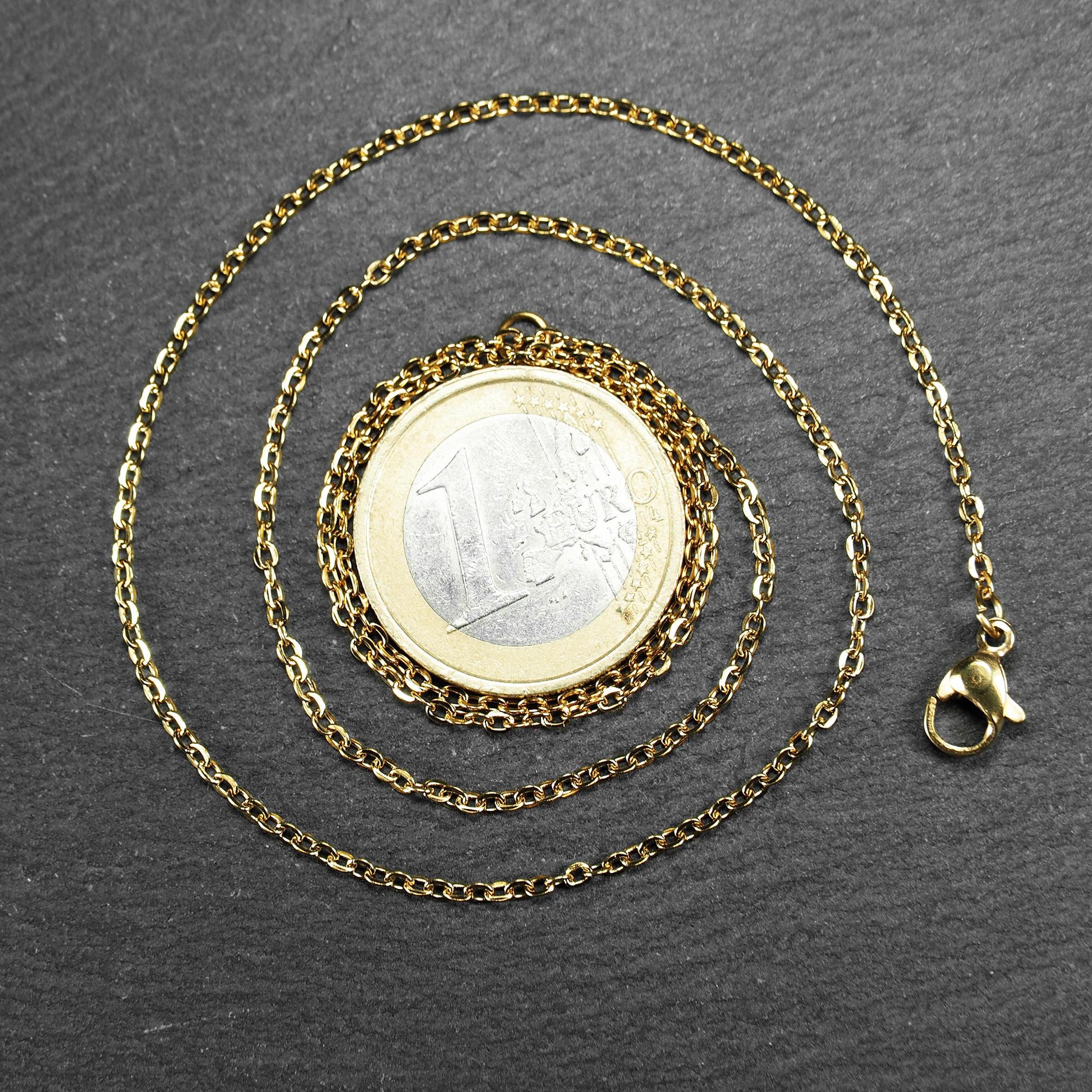 Feine goldfarbene Ankerkette mit glänzender Oberfläche, filigranen ovalen Gliedern in Spiralform und sichtbarem Karabinerverschluss.