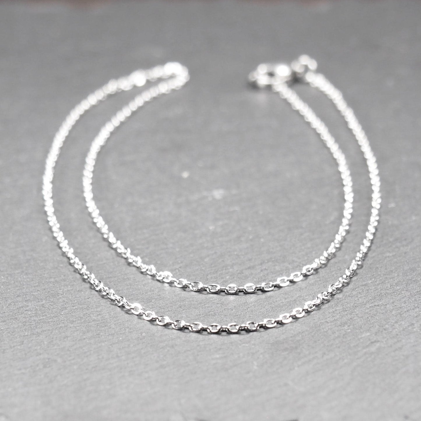 Eine Ankerkette hat filigrane offene Ankerglieder, polierte silberne Oberfläche und einen sichtbaren Karabinerverschluss.