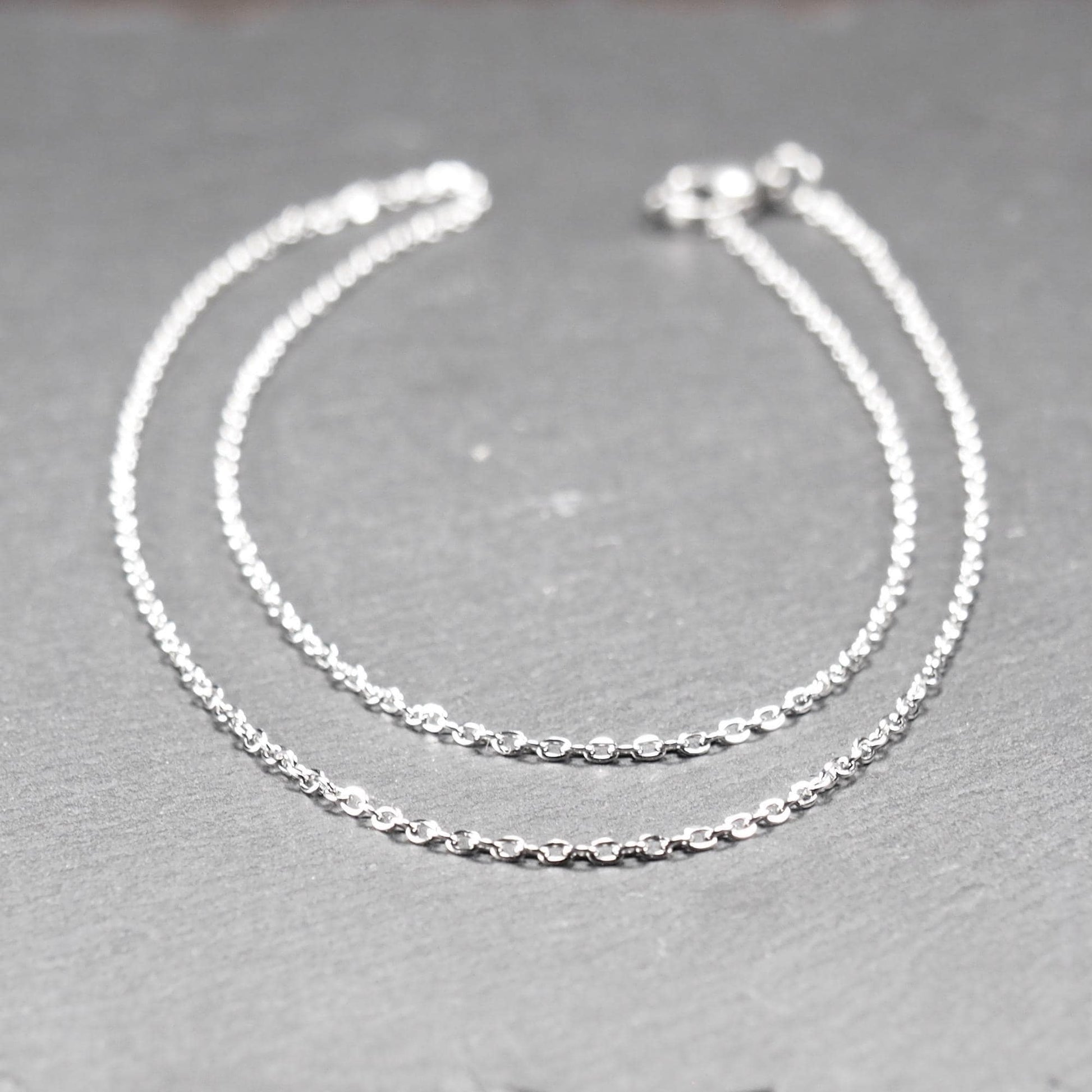 Eine Ankerkette hat filigrane offene Ankerglieder, polierte silberne Oberfläche und einen sichtbaren Karabinerverschluss.