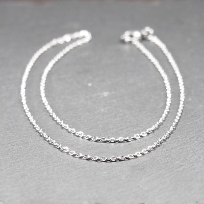 Eine Ankerkette hat filigrane offene Ankerglieder, polierte silberne Oberfläche und einen sichtbaren Karabinerverschluss.