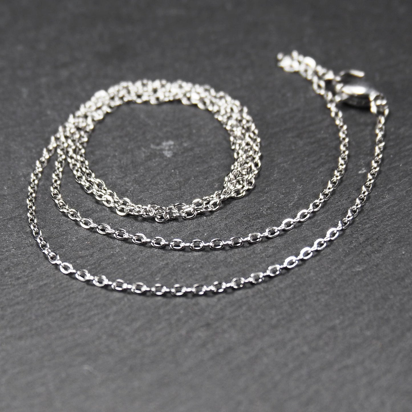 Eine Ankerkette hat filigrane offene Ankerglieder, polierte silberne Oberfläche und einen sichtbaren Karabinerverschluss.