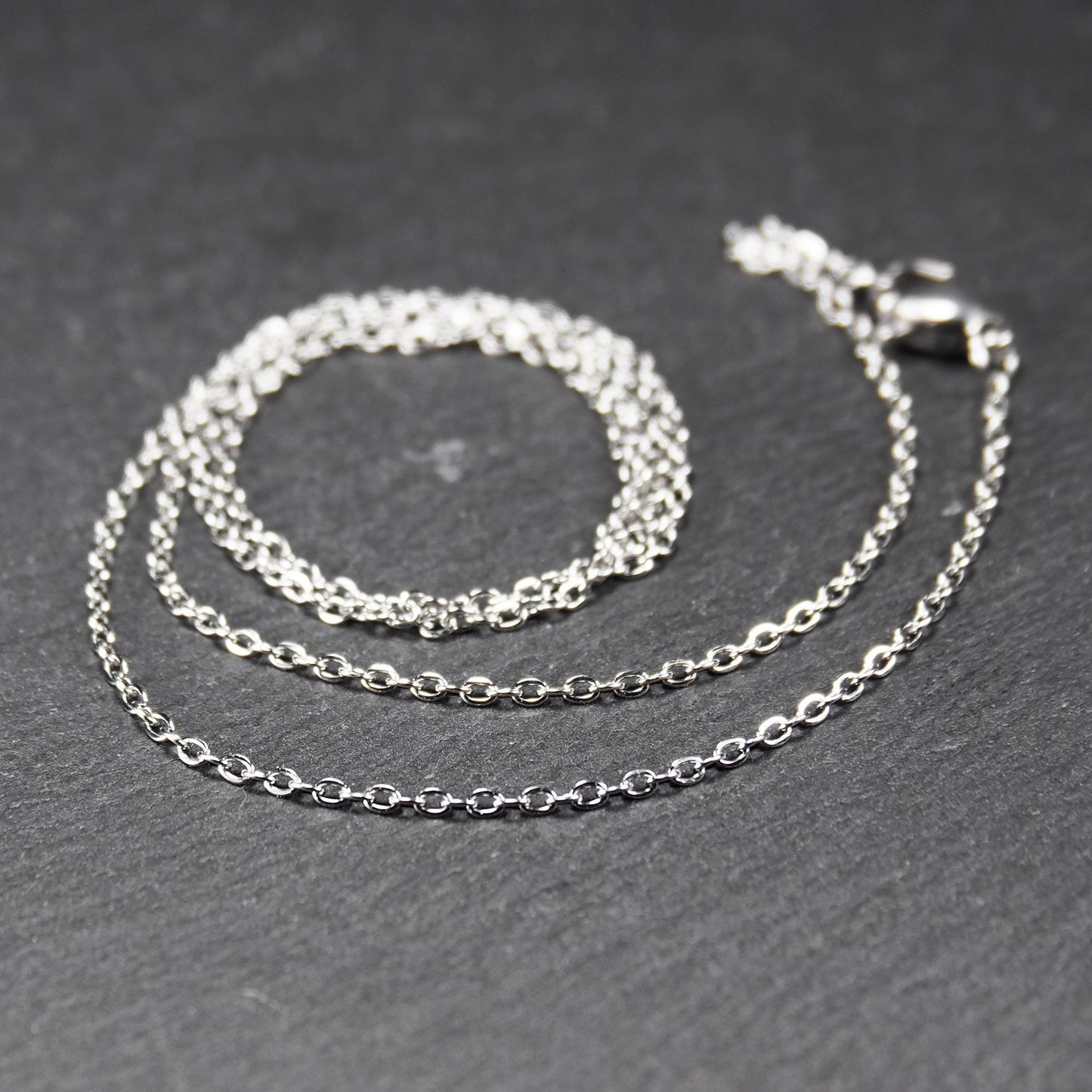 Eine Ankerkette hat filigrane offene Ankerglieder, polierte silberne Oberfläche und einen sichtbaren Karabinerverschluss.