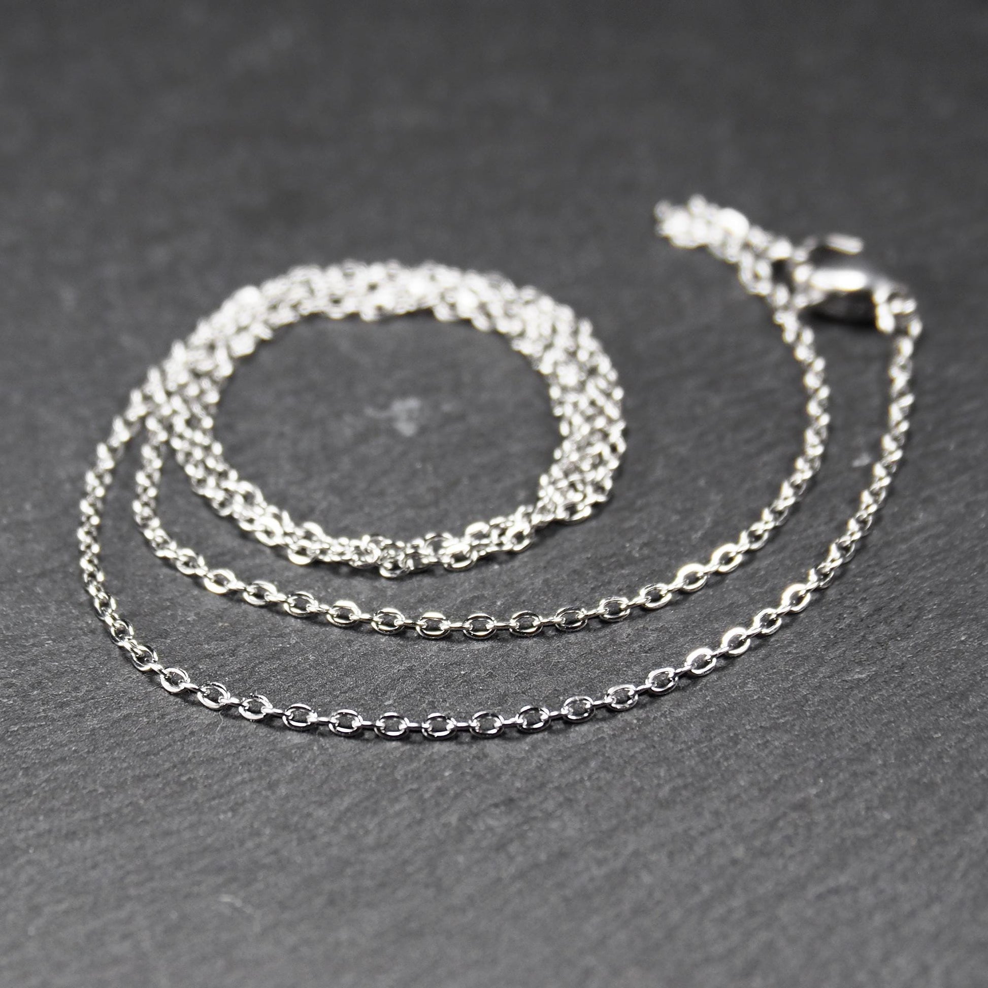 Eine Ankerkette hat filigrane offene Ankerglieder, polierte silberne Oberfläche und einen sichtbaren Karabinerverschluss.