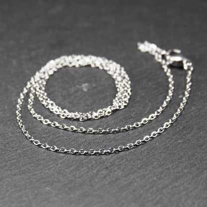 Eine Ankerkette hat filigrane offene Ankerglieder, polierte silberne Oberfläche und einen sichtbaren Karabinerverschluss.