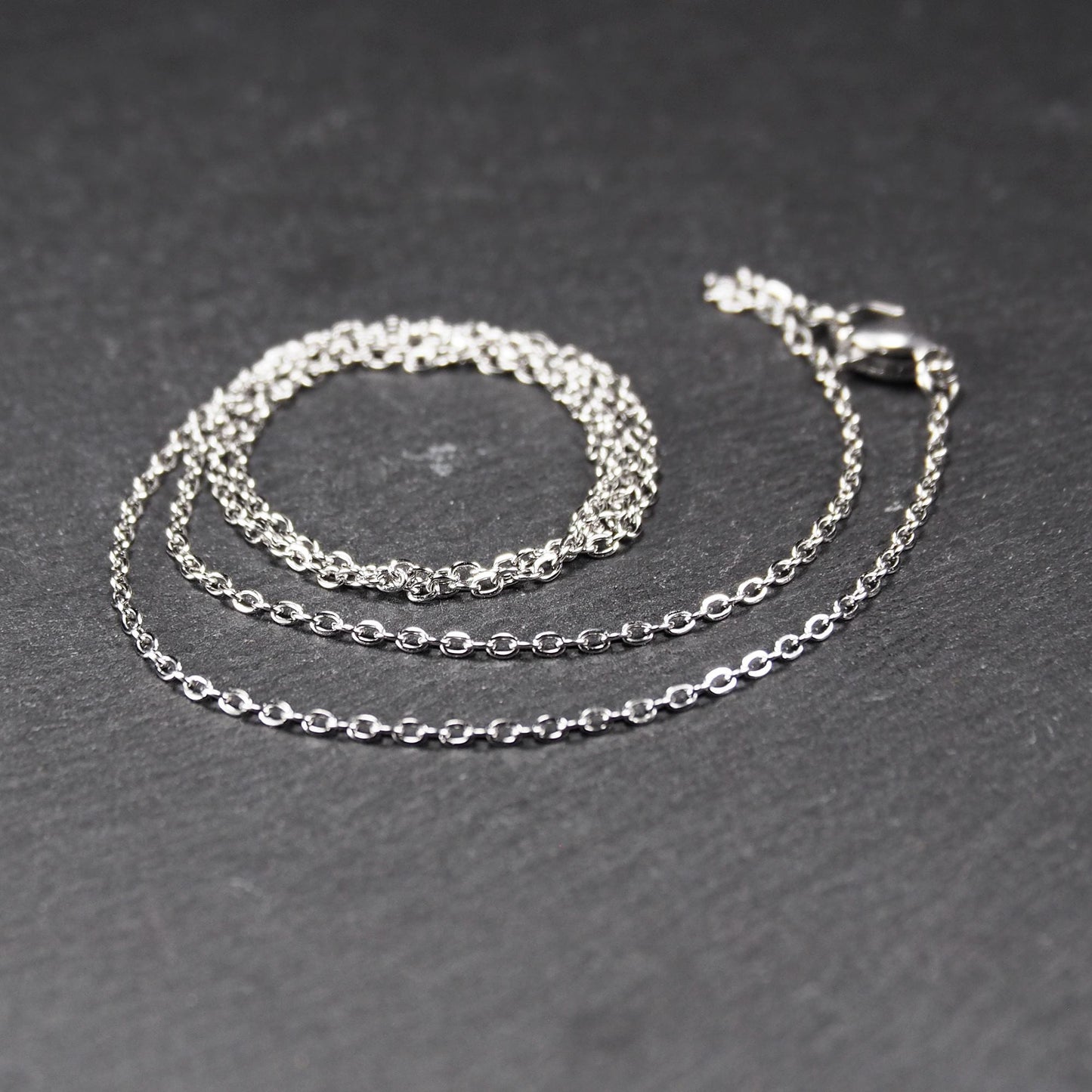 Eine Ankerkette hat filigrane offene Ankerglieder, polierte silberne Oberfläche und einen sichtbaren Karabinerverschluss.