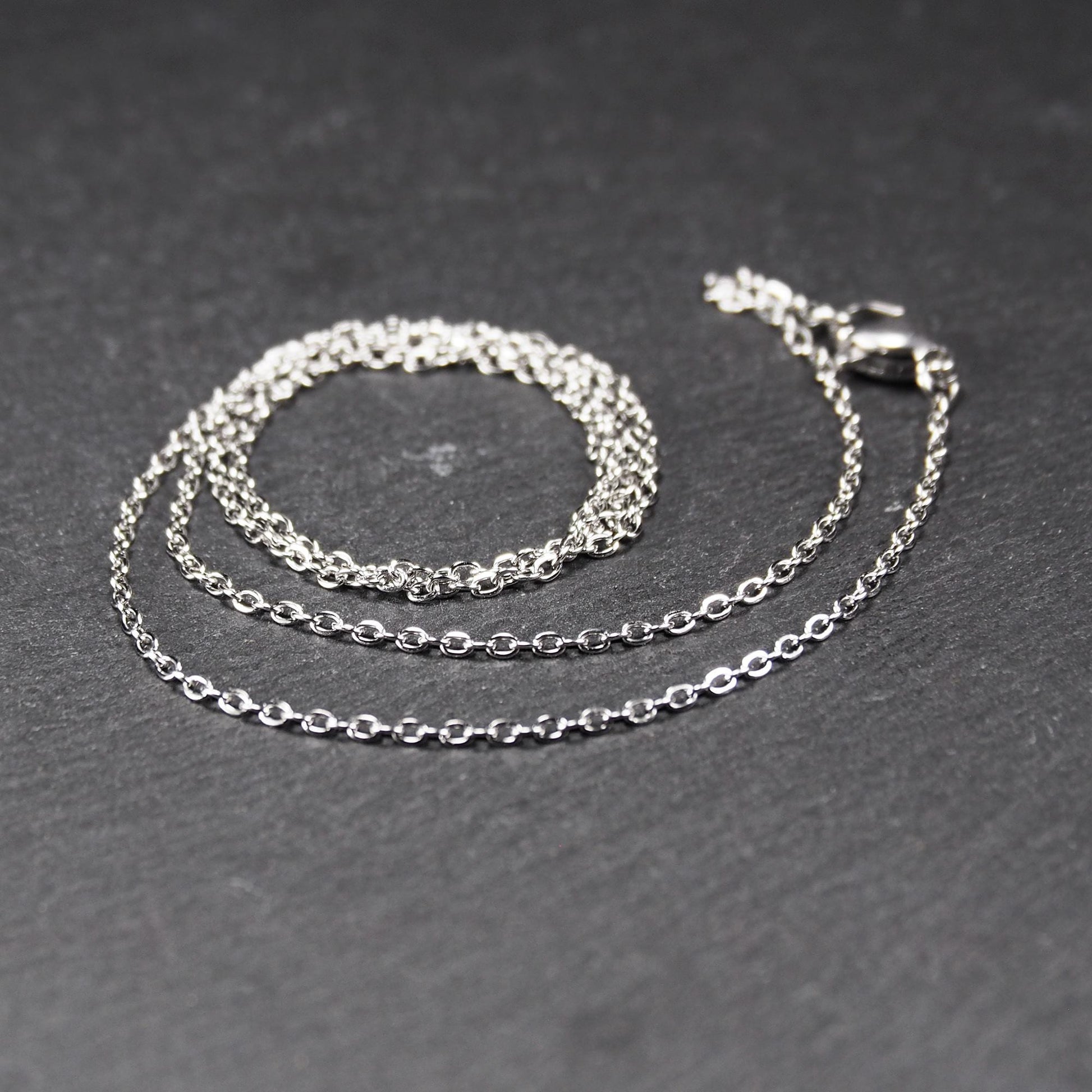 Eine Ankerkette hat filigrane offene Ankerglieder, polierte silberne Oberfläche und einen sichtbaren Karabinerverschluss.