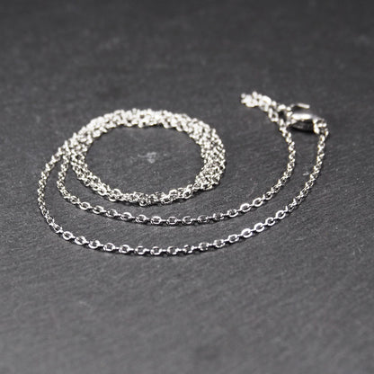 Eine Ankerkette hat filigrane offene Ankerglieder, polierte silberne Oberfläche und einen sichtbaren Karabinerverschluss.