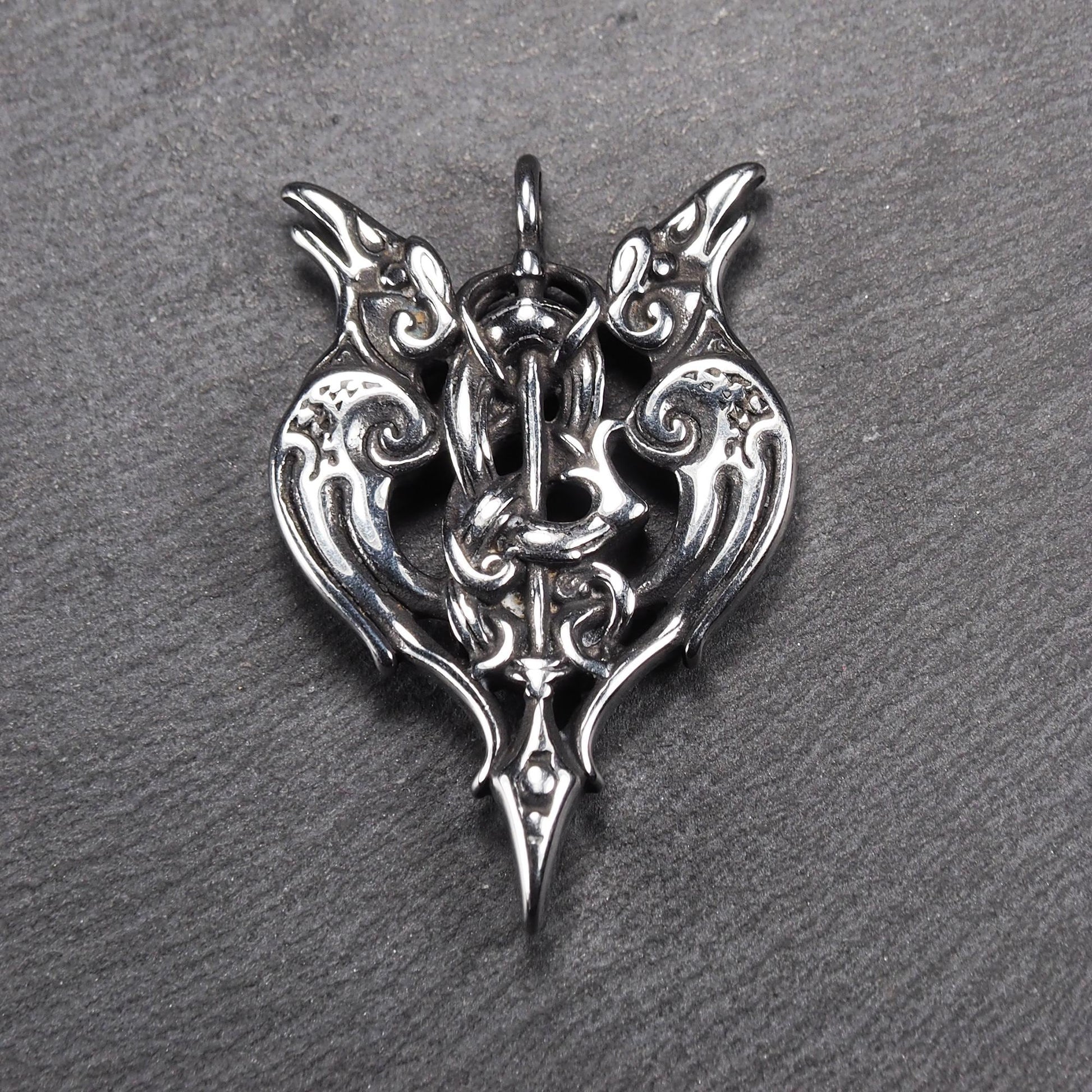 Anhänger aus poliertem silberfarbenem Edelstahl, zweiköpfiges, spitz zulaufendes Rabenschwert Ornament mit Relief, Durchbrüchen und sichtbarer Öse.