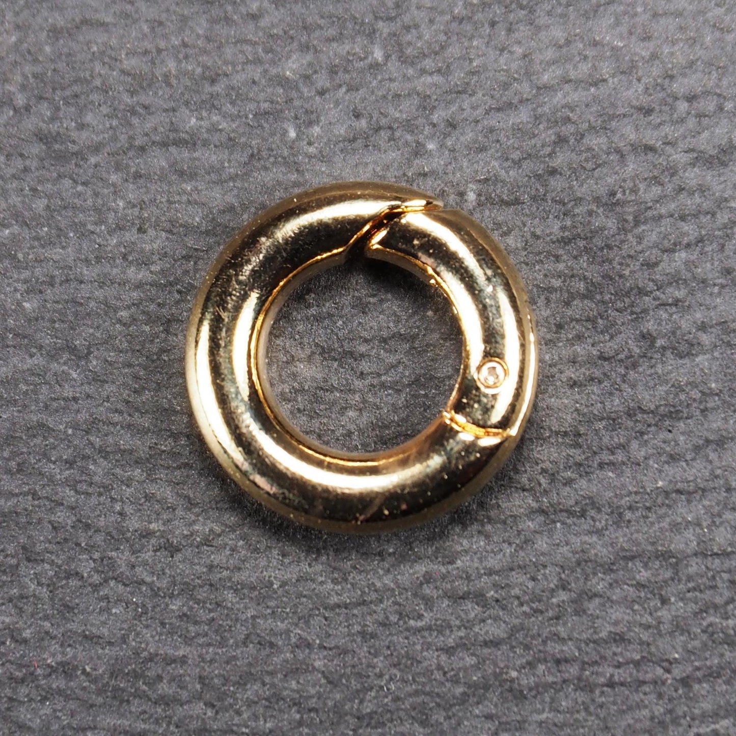 Runder vergoldeter O-Ring Karabiner mit glänzender Oberfläche, torusförmiger Öffnung und sichtbarem Schnappverschluss mit Scharnier.