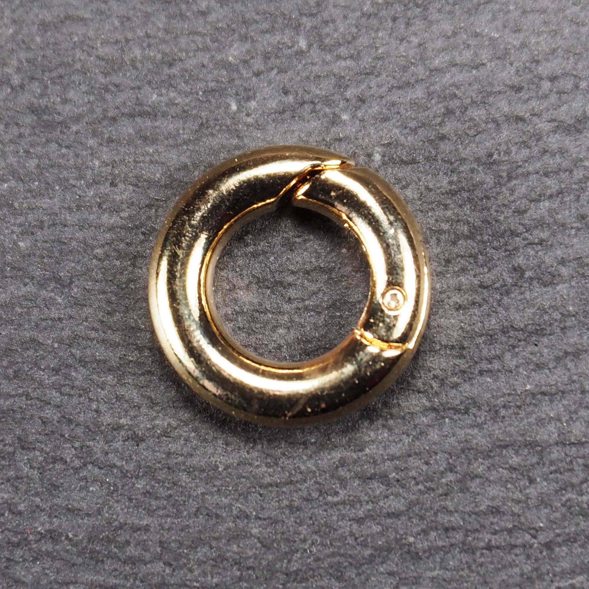 Runder vergoldeter O-Ring Karabiner mit glänzender Oberfläche, torusförmiger Öffnung und sichtbarem Schnappverschluss mit Scharnier.