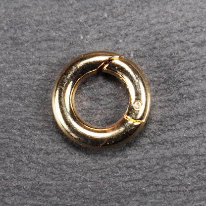 Runder vergoldeter O-Ring Karabiner mit glänzender Oberfläche, torusförmiger Öffnung und sichtbarem Schnappverschluss mit Scharnier.