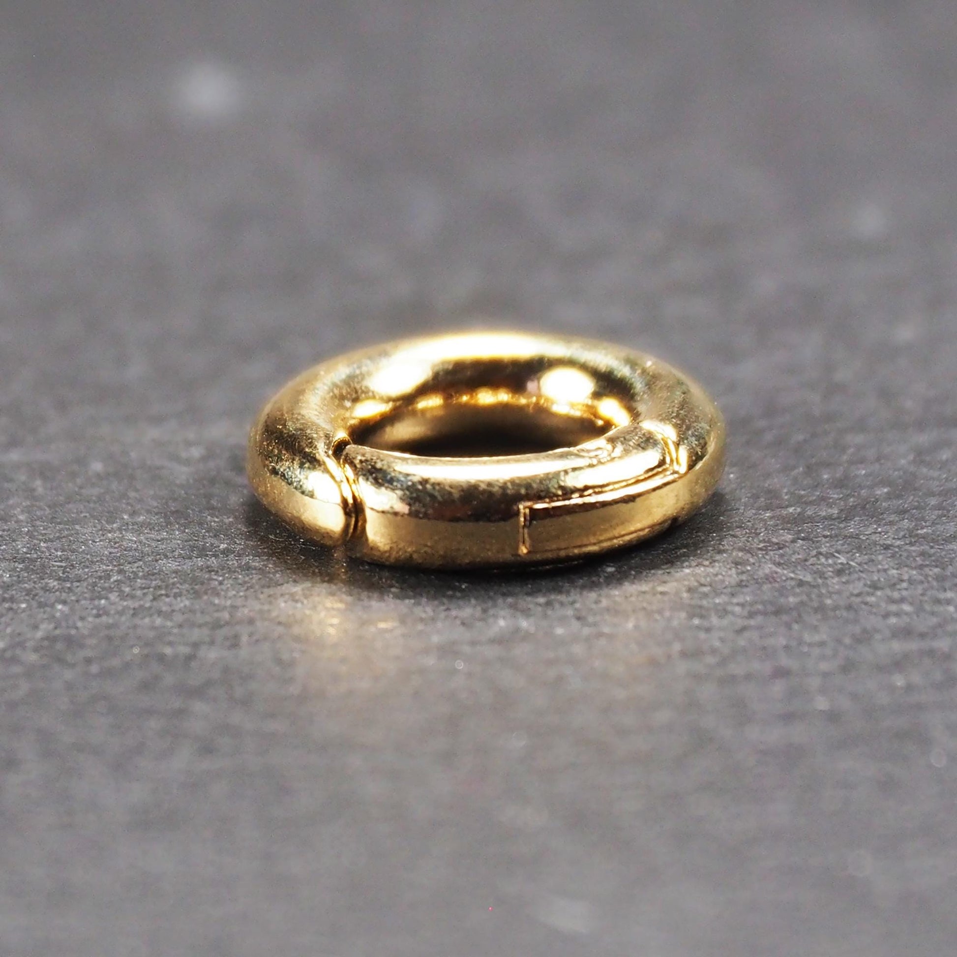 Runder vergoldeter O-Ring Karabiner mit glänzender Oberfläche, torusförmiger Öffnung und sichtbarem Schnappverschluss mit Scharnier.