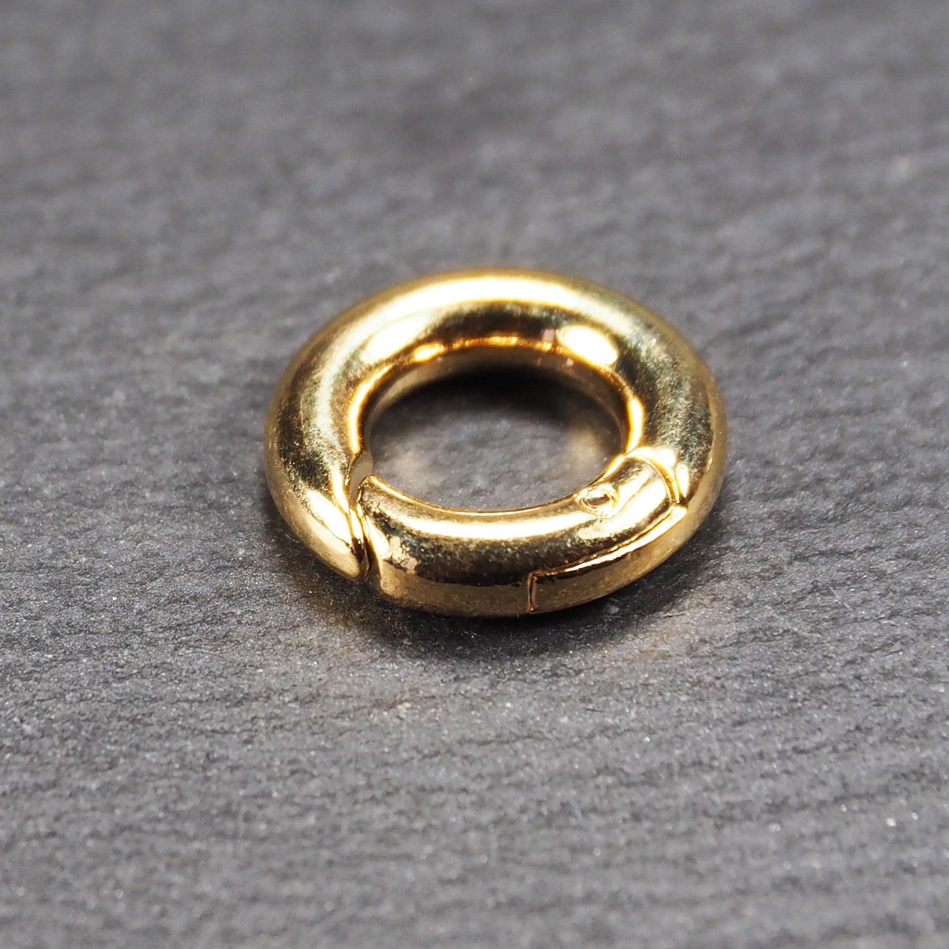 Runder vergoldeter O-Ring Karabiner mit glänzender Oberfläche, torusförmiger Öffnung und sichtbarem Schnappverschluss mit Scharnier.