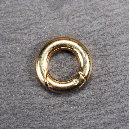 Runder vergoldeter O-Ring Karabiner mit glänzender Oberfläche, torusförmiger Öffnung und sichtbarem Schnappverschluss mit Scharnier.