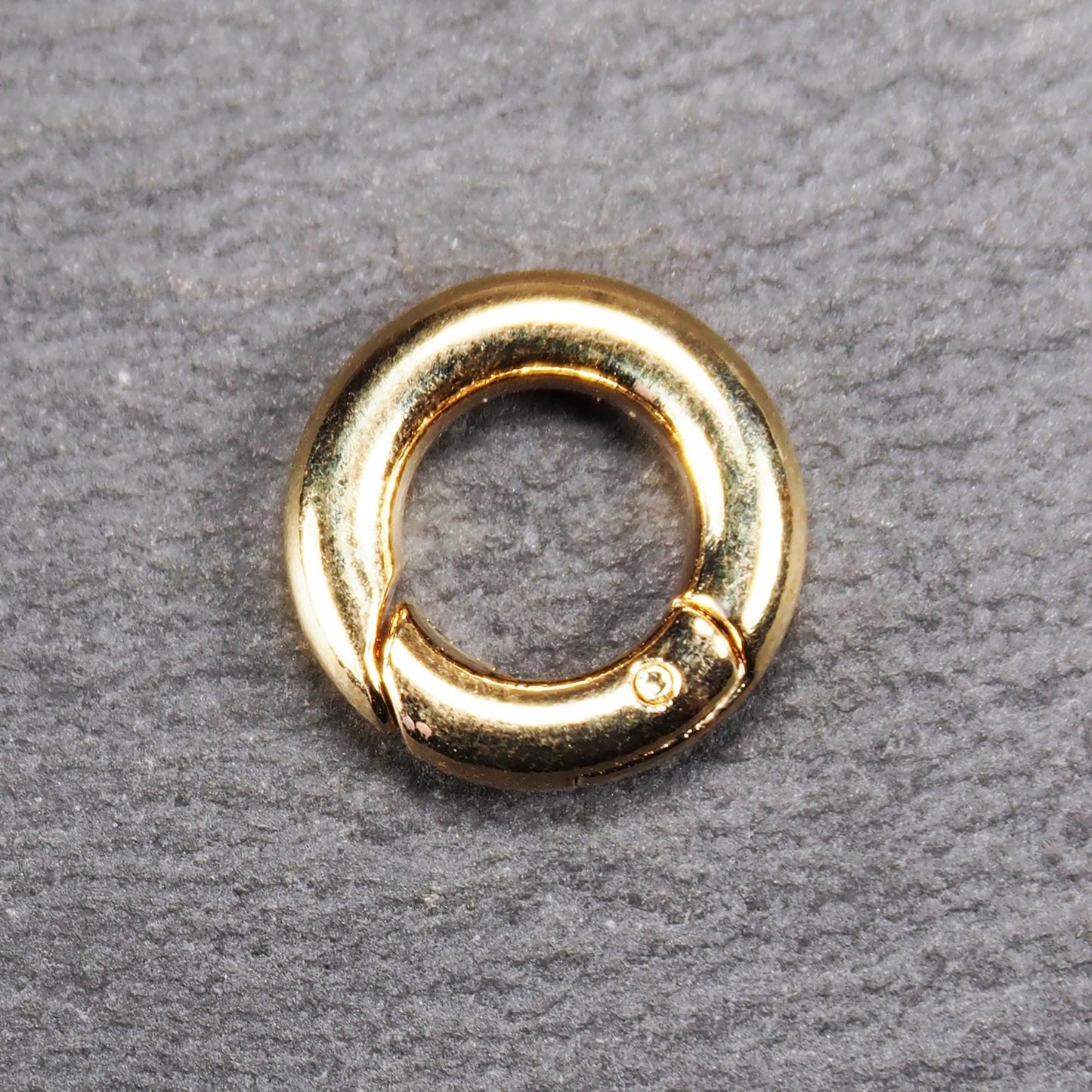 Runder vergoldeter O-Ring Karabiner mit glänzender Oberfläche, torusförmiger Öffnung und sichtbarem Schnappverschluss mit Scharnier.