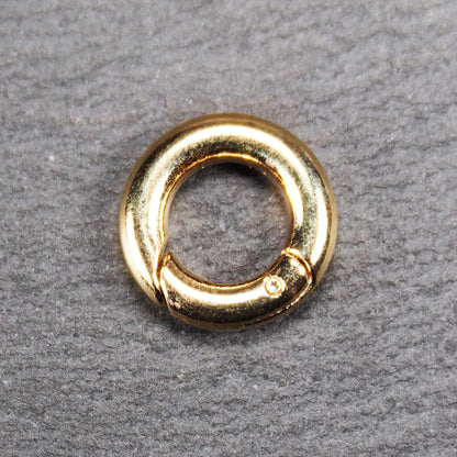 Runder vergoldeter O-Ring Karabiner mit glänzender Oberfläche, torusförmiger Öffnung und sichtbarem Schnappverschluss mit Scharnier.