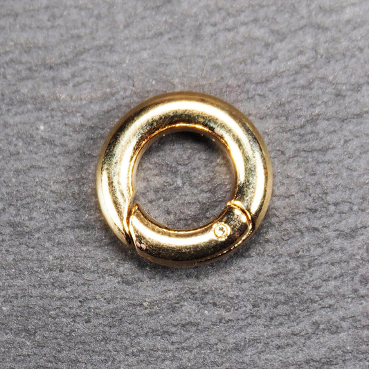 Runder vergoldeter O-Ring Karabiner mit glänzender Oberfläche, torusförmiger Öffnung und sichtbarem Schnappverschluss mit Scharnier.