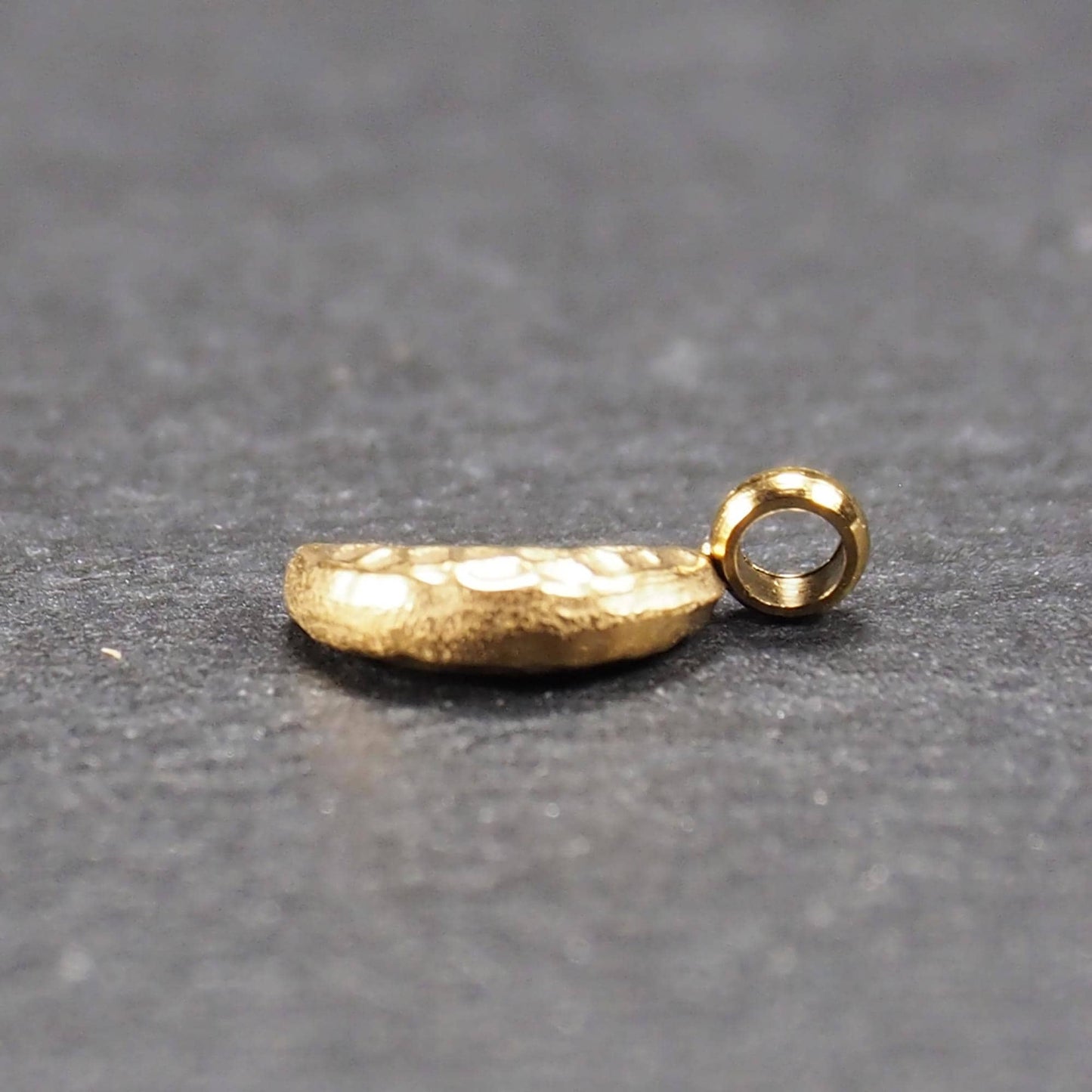 Halbmond-Anhänger, goldfarben und glänzend, reliefartige gehämmerte Textur, organisch geschwungene Mondsichelform mit kleiner Öse oben.