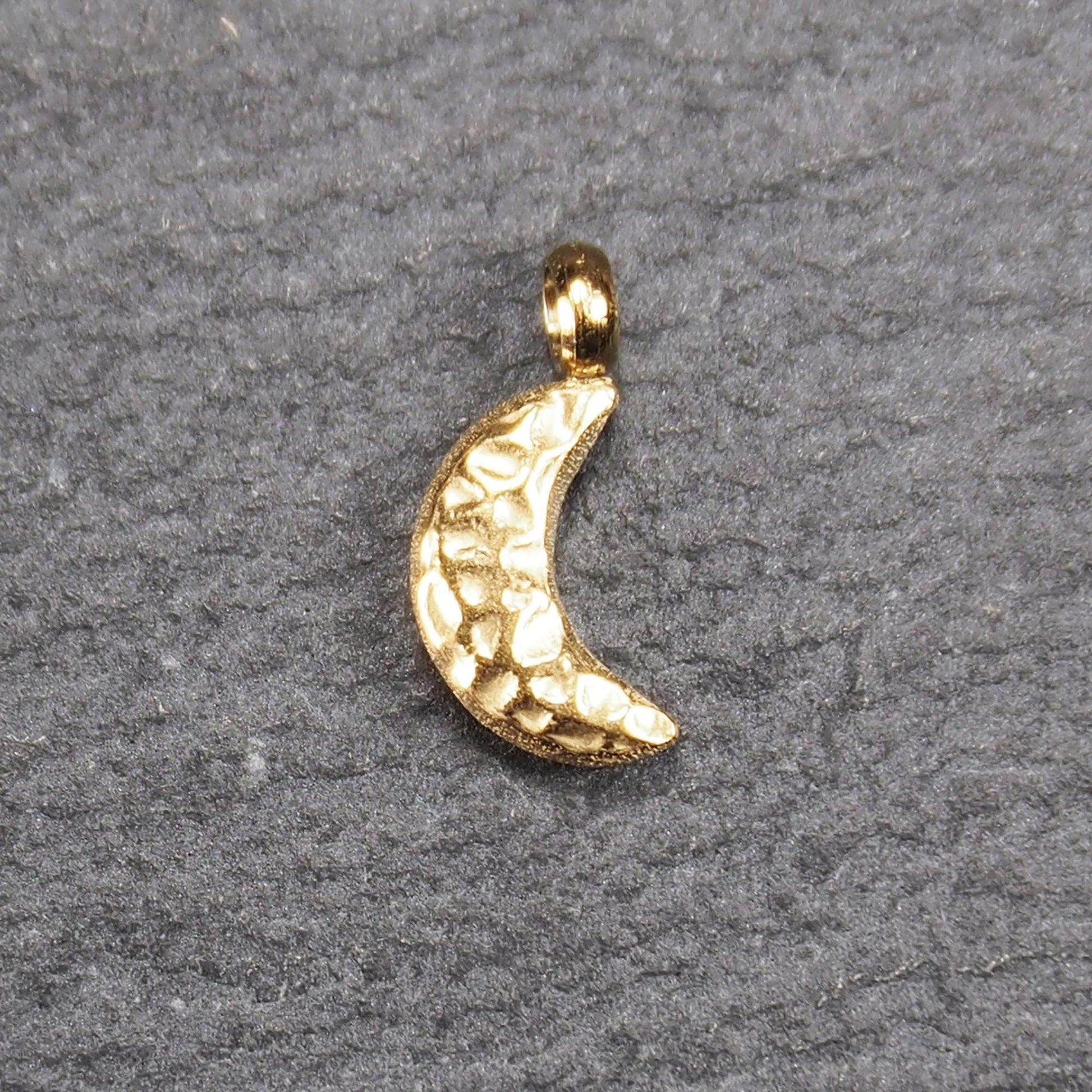 Halbmond-Anhänger, goldfarben und glänzend, reliefartige gehämmerte Textur, organisch geschwungene Mondsichelform mit kleiner Öse oben.