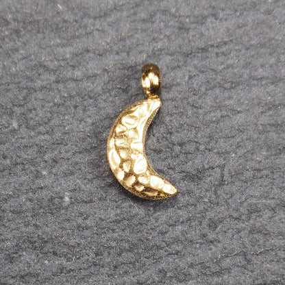 Halbmond-Anhänger, goldfarben und glänzend, reliefartige gehämmerte Textur, organisch geschwungene Mondsichelform mit kleiner Öse oben.