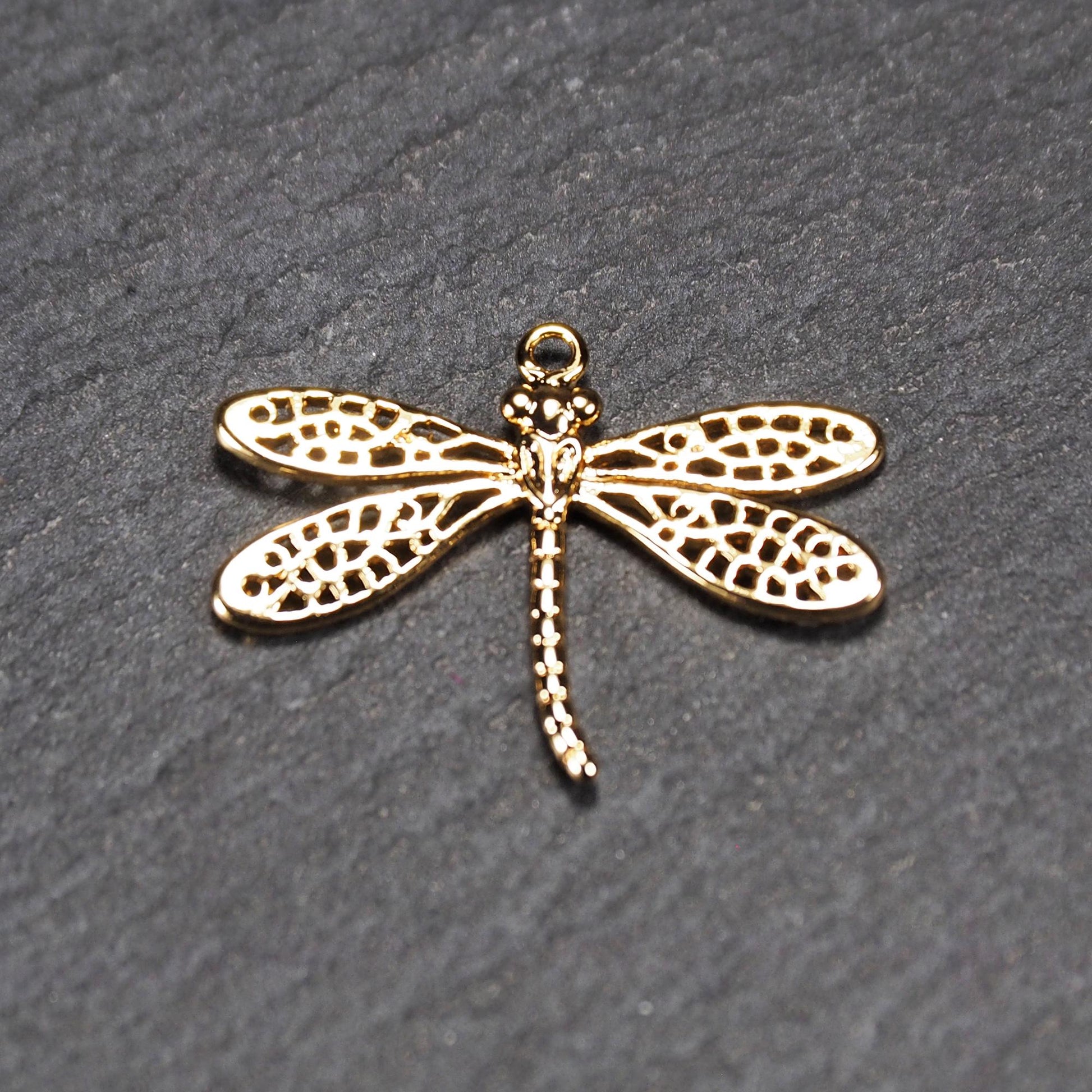 Libellen-Anhänger aus goldfarbenem, glänzendem Metall mit durchbrochenen, netzartigen Flügeln, schlankem segmentiertem Körper und kleiner runder Aufhängöse.