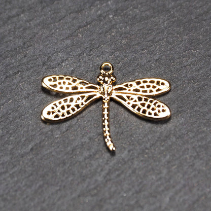 Libellen-Anhänger aus goldfarbenem, glänzendem Metall mit durchbrochenen, netzartigen Flügeln, schlankem segmentiertem Körper und kleiner runder Aufhängöse.