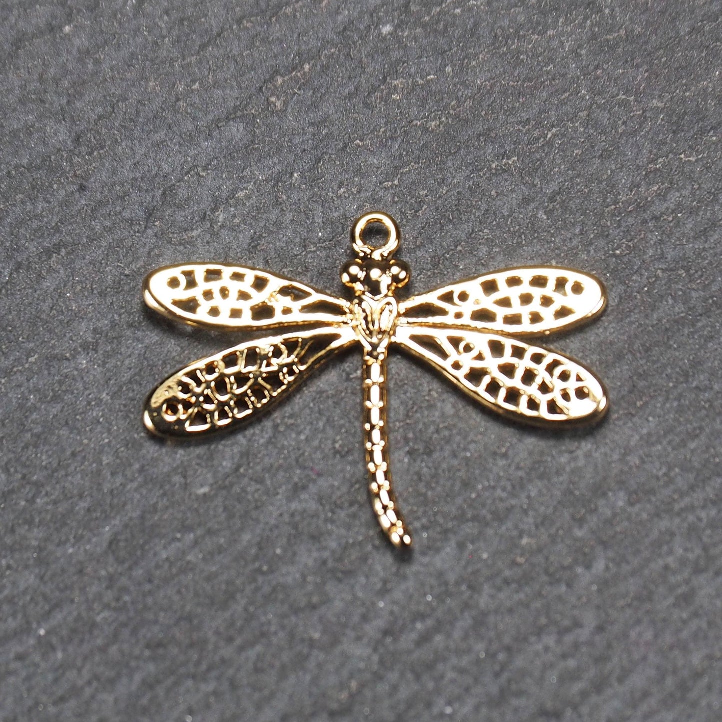 Libellen-Anhänger aus goldfarbenem, glänzendem Metall mit durchbrochenen, netzartigen Flügeln, schlankem segmentiertem Körper und kleiner runder Aufhängöse.