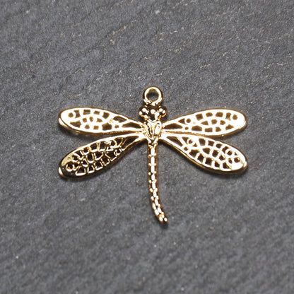 Libellen-Anhänger aus goldfarbenem, glänzendem Metall mit durchbrochenen, netzartigen Flügeln, schlankem segmentiertem Körper und kleiner runder Aufhängöse.