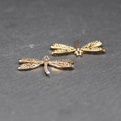 Libellen-Anhänger (Vorder- und Rückseite) aus goldfarbenem, glänzendem Metall mit durchbrochenen, netzartigen Flügeln, schlankem segmentiertem Körper und kleiner runder Aufhängöse.